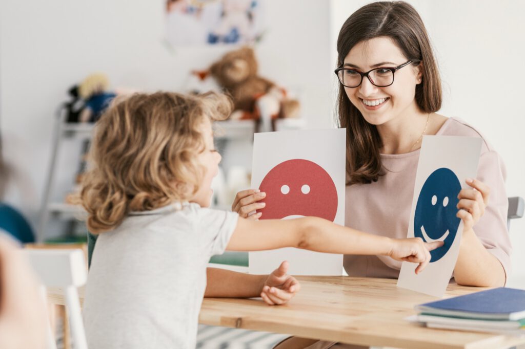 Child identifying emotions using smiley face cards during a therapy session with a child psychologist